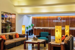 Un vestíbulo con sofá, sillas, una mesa de centro y una recepción con panel de madera y señalización de 'Fiesta Inn'.