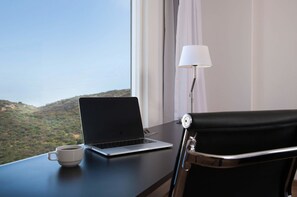 A laptop on a desk with a cup of coffee, a lamp, and a view of a mountainous landscape through a window. - Fiesta Inn Tuxtla (Tuxtla Gutierrez)