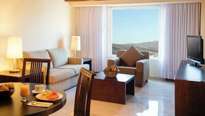Habitación de hotel con sofá, sillón, mesa de comedor y televisor.