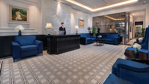 A modern lobby with a reception desk, blue seating, patterned flooring, and decorative wall art.
