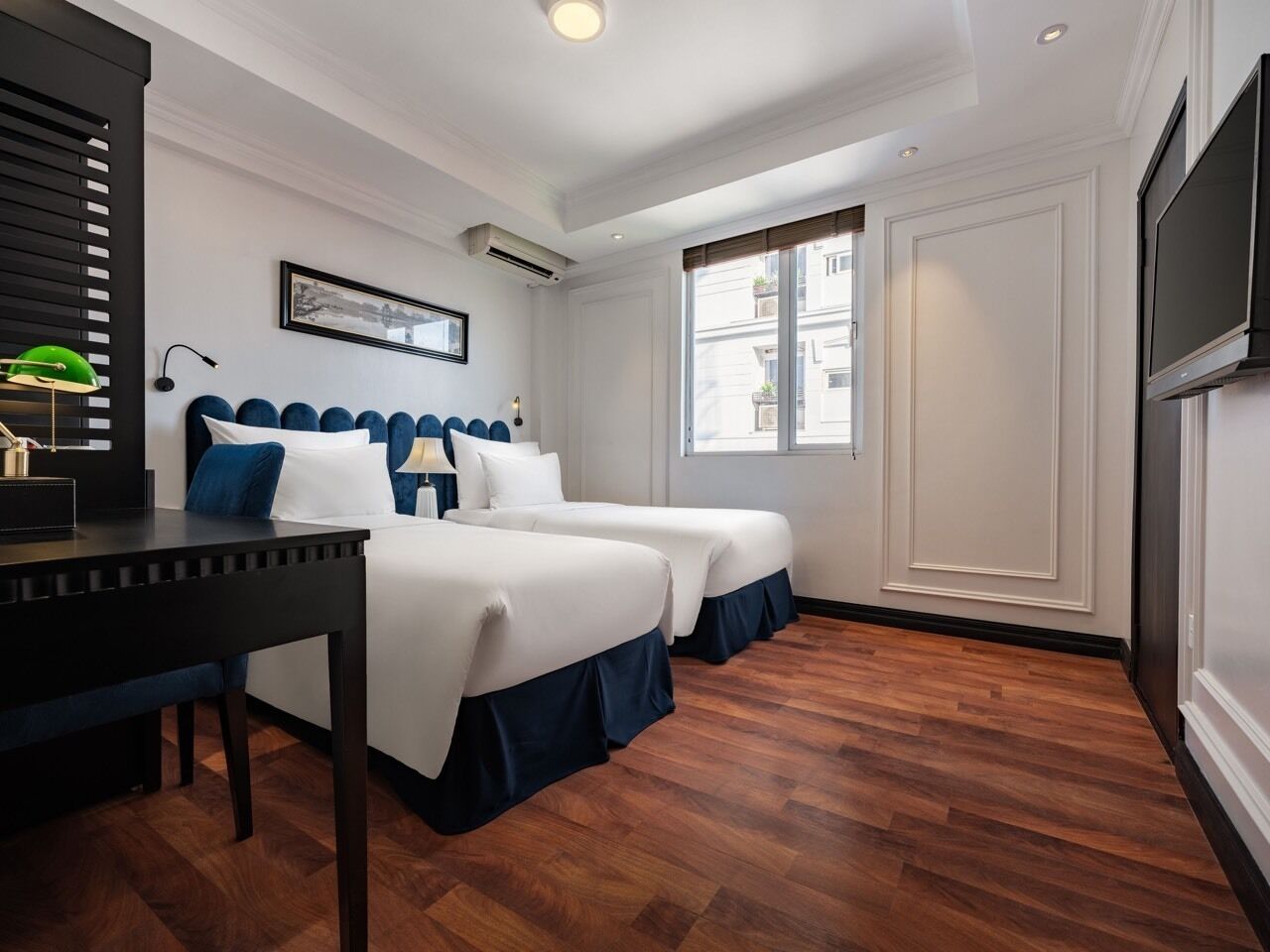 Een hotelkamer met twee bedden, een bureau, een televisie en een groot raam.