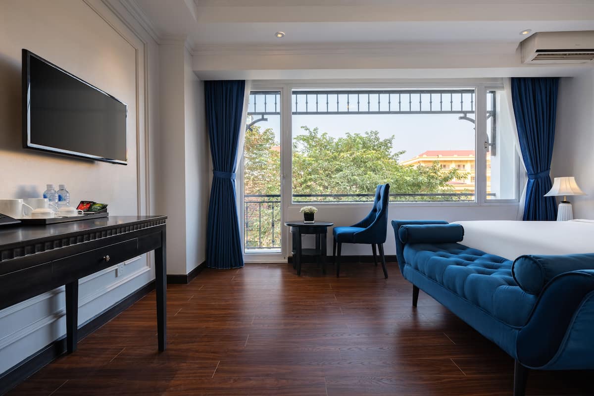 Una habitación de hotel con cama, escritorio con televisor, una silla y balcón con vistas.