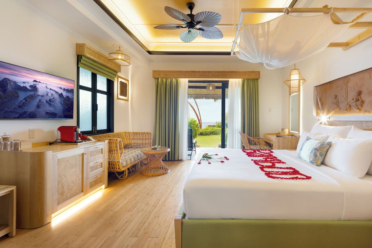 A hotel room with a large bed, a television, a desk with a computer, and a view of the outdoors.
