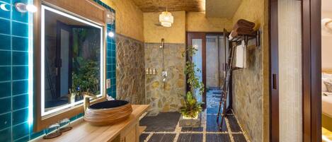 Une salle de bain avec un mur en pierre, un meuble-lavabo en bois, un grand miroir et un espace douche.