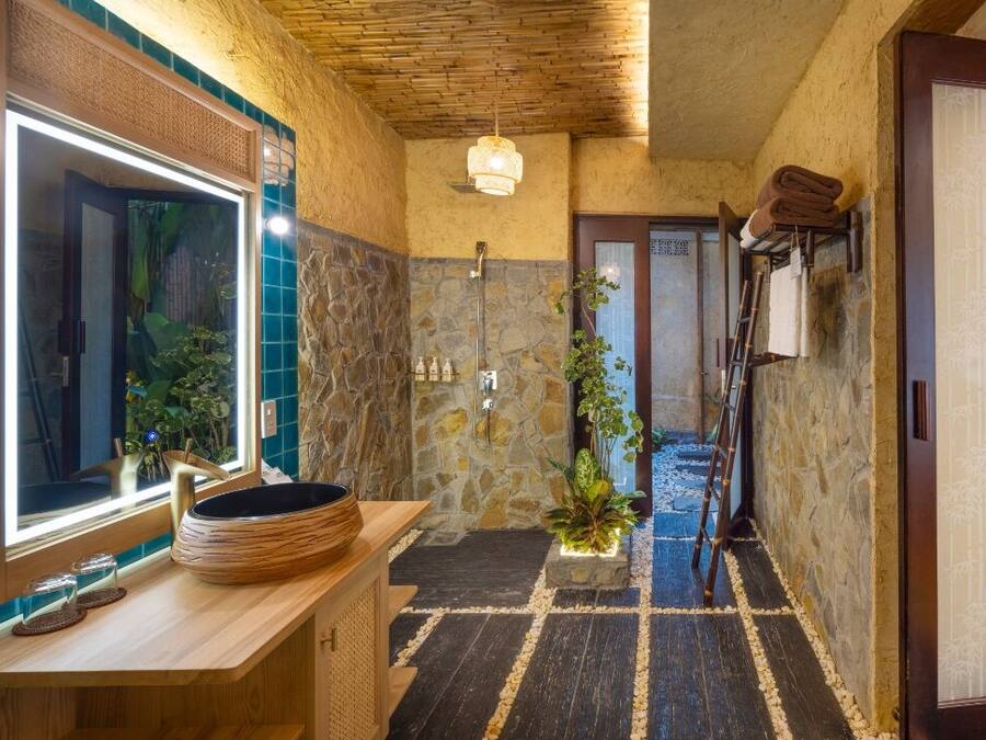 A bathroom with a stone wall, a wooden vanity, a large mirror, and a shower area.