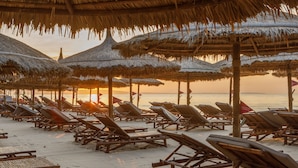 Una playa con hileras de sillas de madera y sombrillas de paja, dispuestas para tomar el sol.