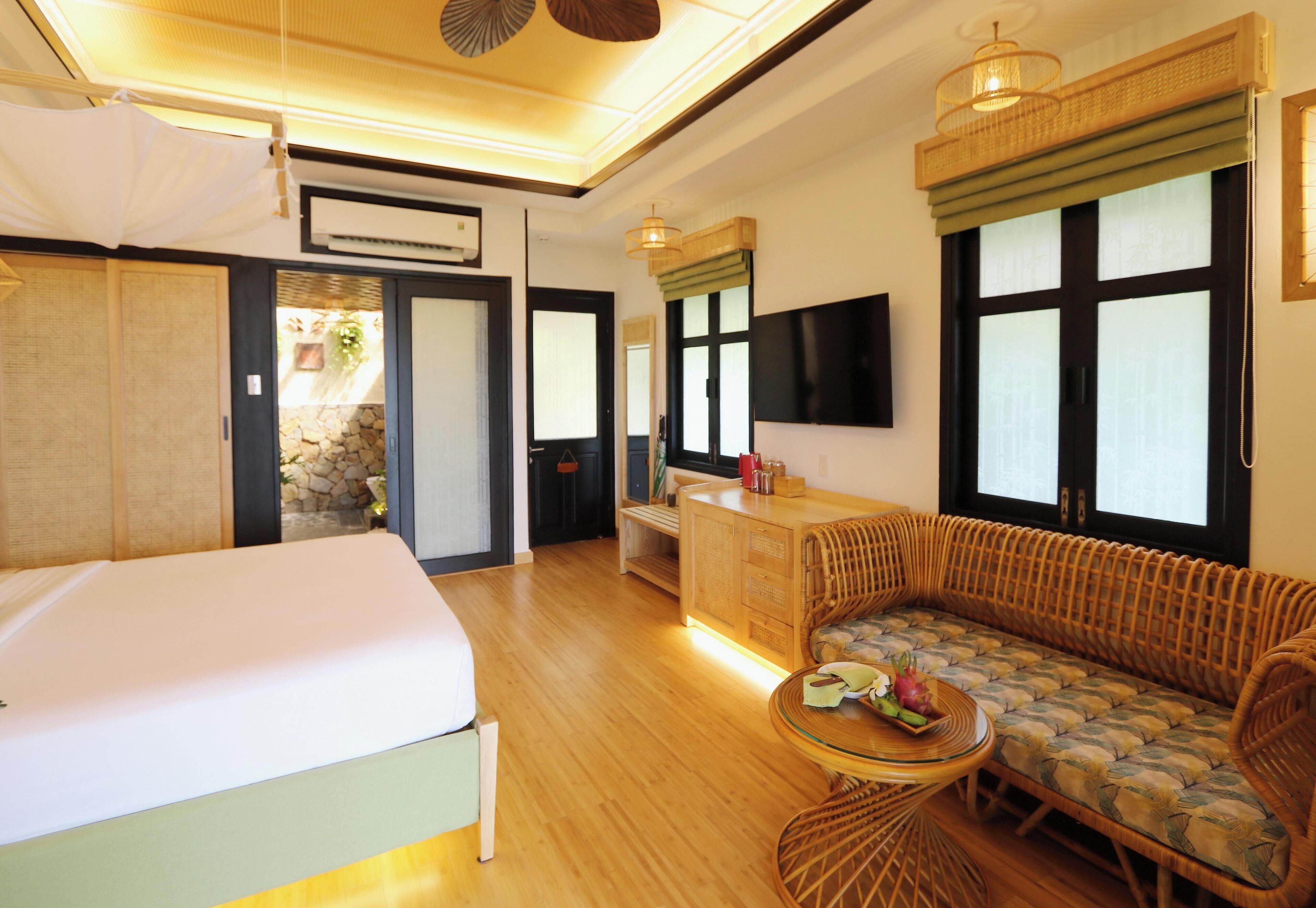 A hotel room with a bed, a sofa, a small table, a TV, and a window with blinds.