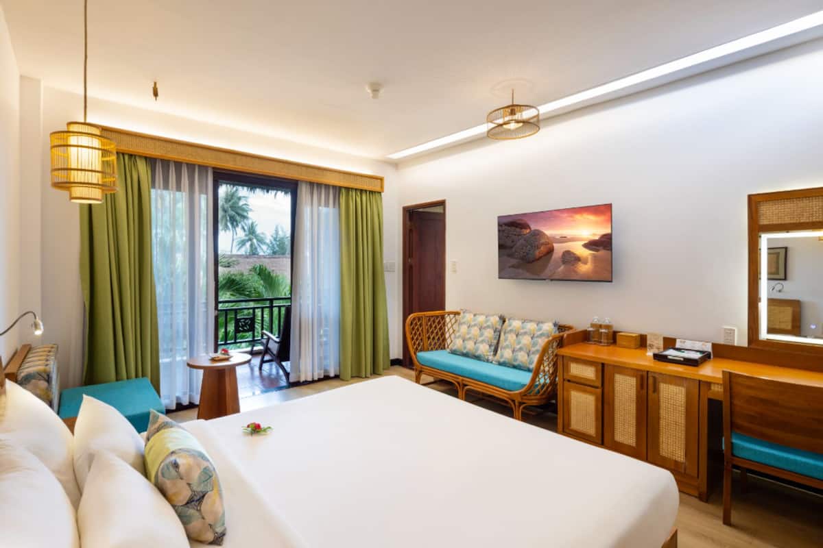 A hotel room with a large bed, a sofa, a desk, and a balcony with curtains.