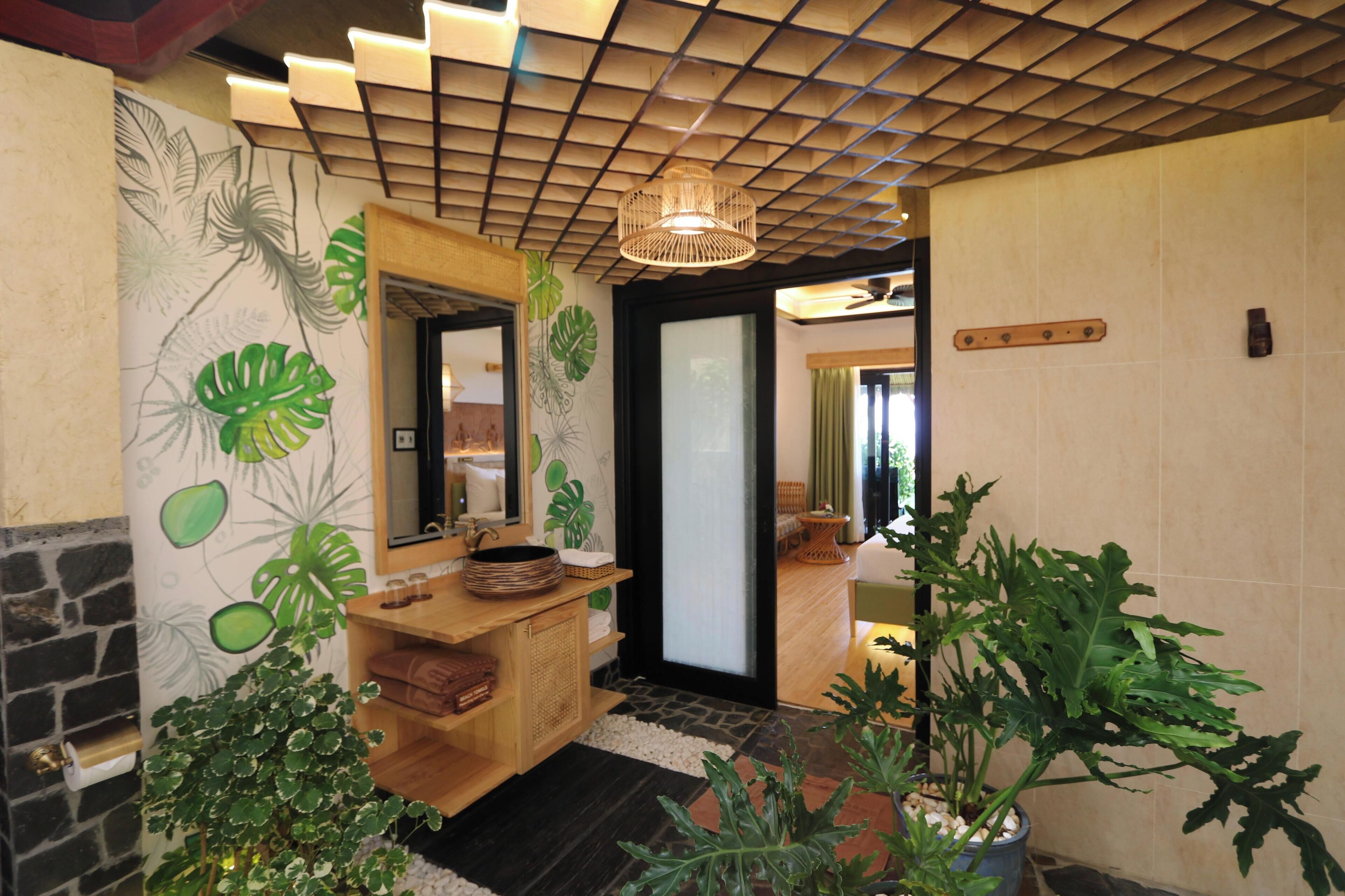 A hotel lobby with a wooden reception desk, a large mirror, and tropical leaf wall art.