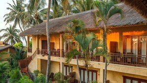 Un hotel de varios pisos con techo de paja, balcones con barandillas de madera y exuberante vegetación tropical.