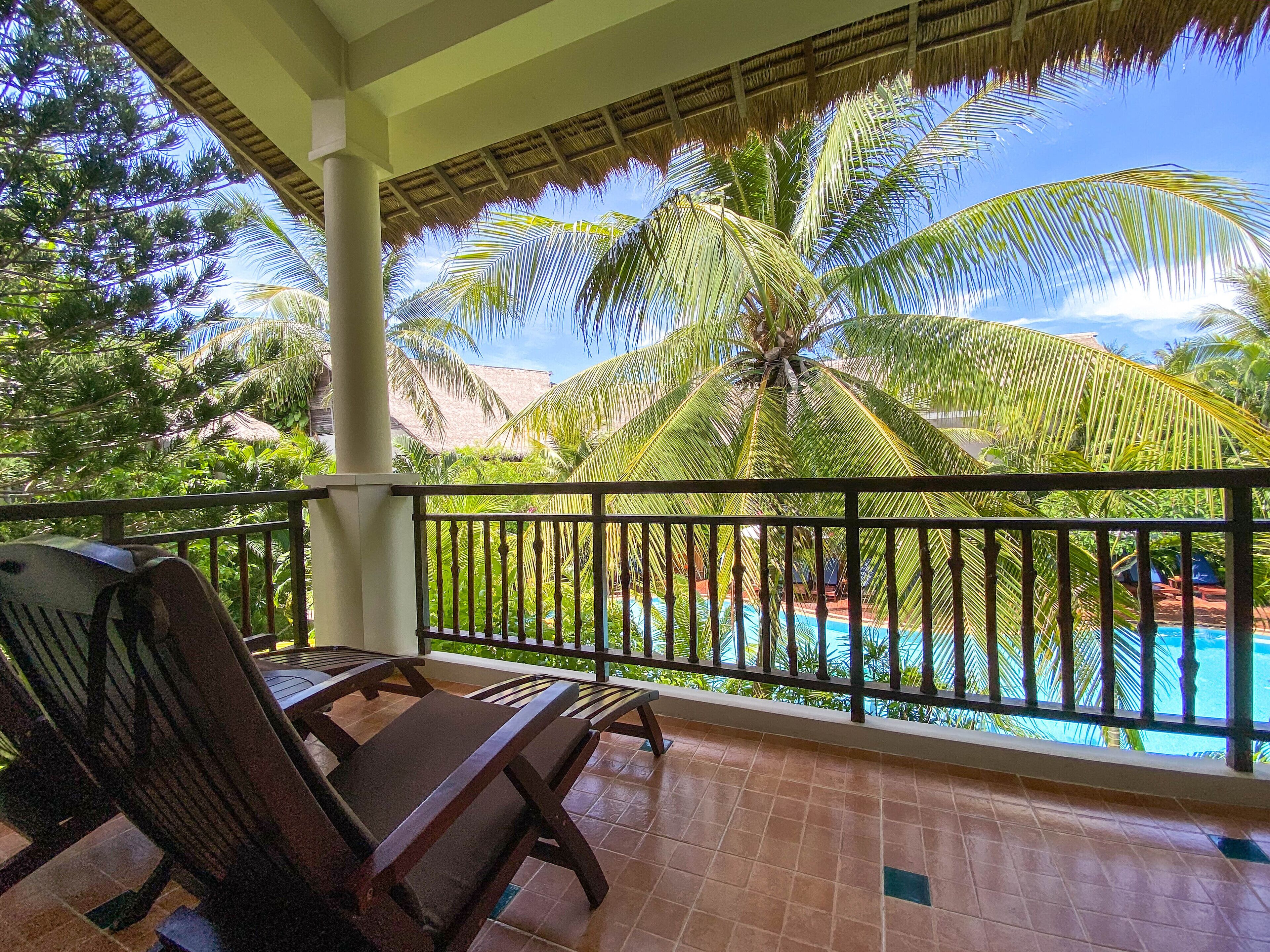 A balcony with a pool, palm trees, and lounge chairs.
