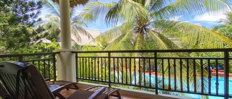 A balcony with a pool, palm trees, and lounge chairs.