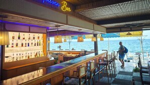 Un bar con vistas al mar, muebles de madera y un letrero de neón.