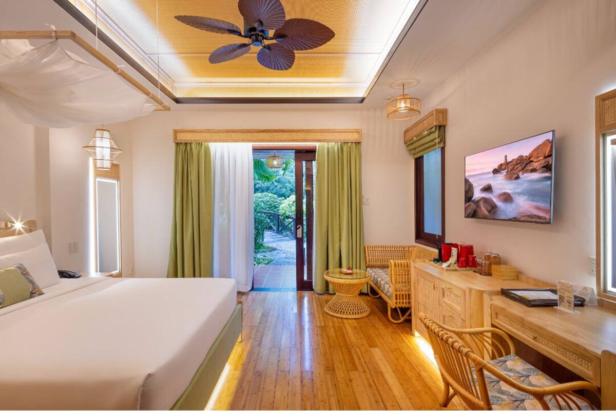 A hotel room with a large bed, a desk with a chair, a ceiling fan, and a view of the outdoors.