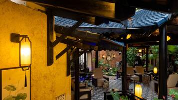 Un espacio al aire libre acogedor con muebles de madera y faroles, rodeado de plantas y un muro de ladrillo.