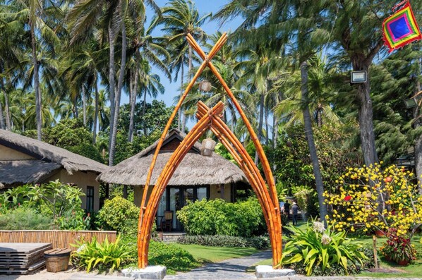 Um resort tropical com cabanas de palha, um arco de bambu e vegetação exuberante.