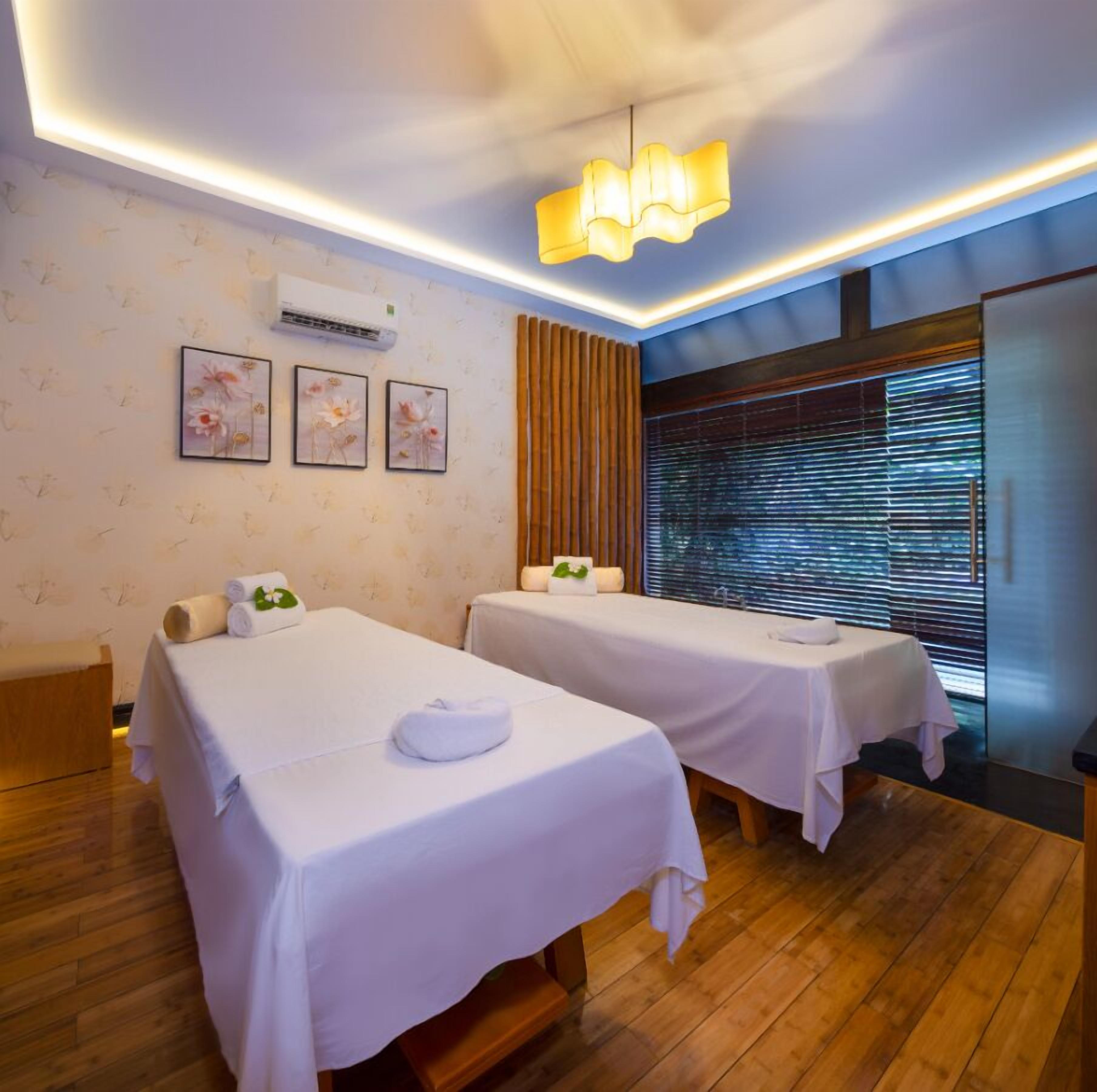 A room with two beds, a wooden floor, a wall-mounted air conditioner, and a window with blinds.