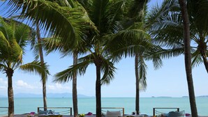 A beachside dining area with wooden tables and chairs, surrounded by palm trees and overlooking the sea. - Samui Palm Beach Lead by Celes Samui (Koh Samui)