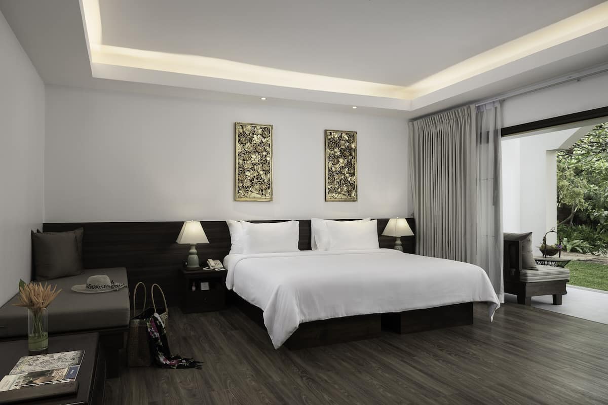 A modern hotel room with a large bed, bedside tables, a sofa, and a view of greenery.