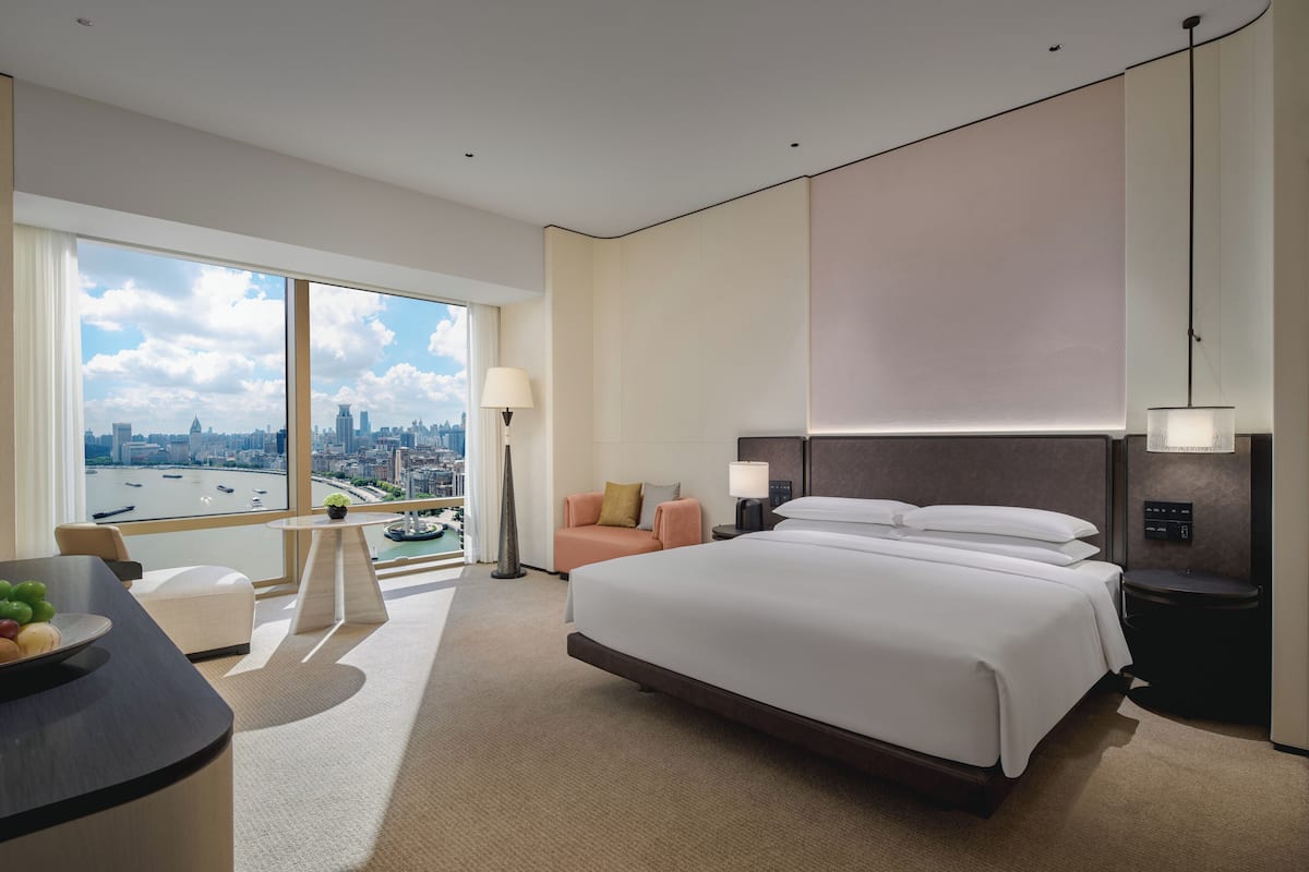 Camera d'albergo con un letto grande, una scrivania, una sedia e vista sulla città attraverso ampie finestre.
