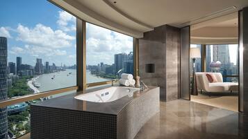 Un baño moderno con una bañera grande, vistas a la ciudad y un sofá en la sala de estar contigua.