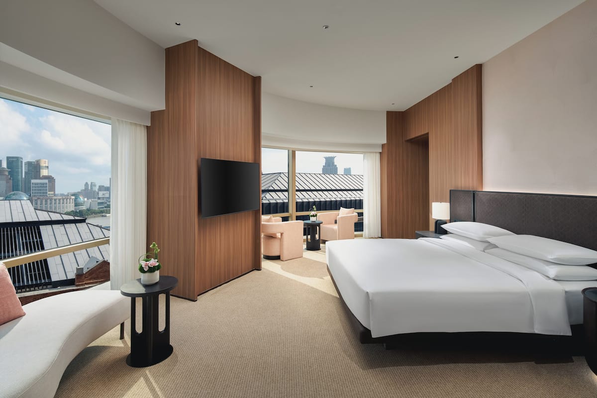 Una moderna camera d'albergo con un letto grande, una TV a schermo piatto, una zona relax con vista sulla città e un balcone affacciato sul panorama urbano.
