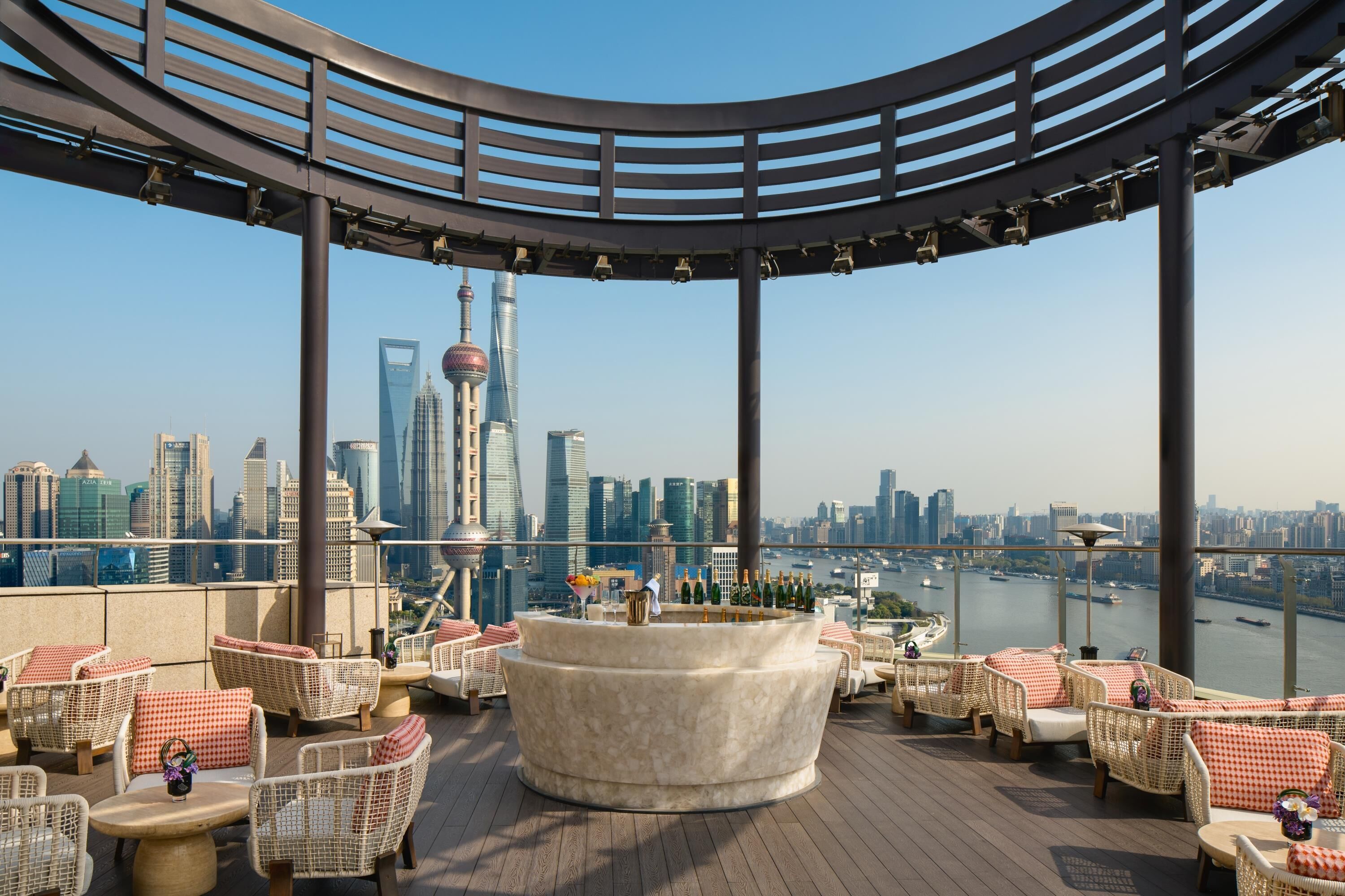 Terraza en la azotea con mobiliario de mimbre, un área de estar central y vistas del horizonte de la ciudad, incluyendo la Torre Perla Oriental.
