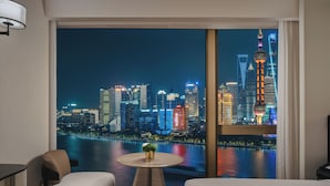 A hotel room with a large window offering a nighttime cityscape view, a round table with a plant, and two upholstered chairs. - Hyatt on the Bund, Shanghai (Shanghai)