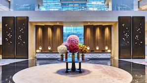 A lobby with a round table surrounded by colorful spherical floral arrangements, a glass ceiling, and a view of the cityscape through large windows. - Hyatt on the Bund, Shanghai (Shanghai)