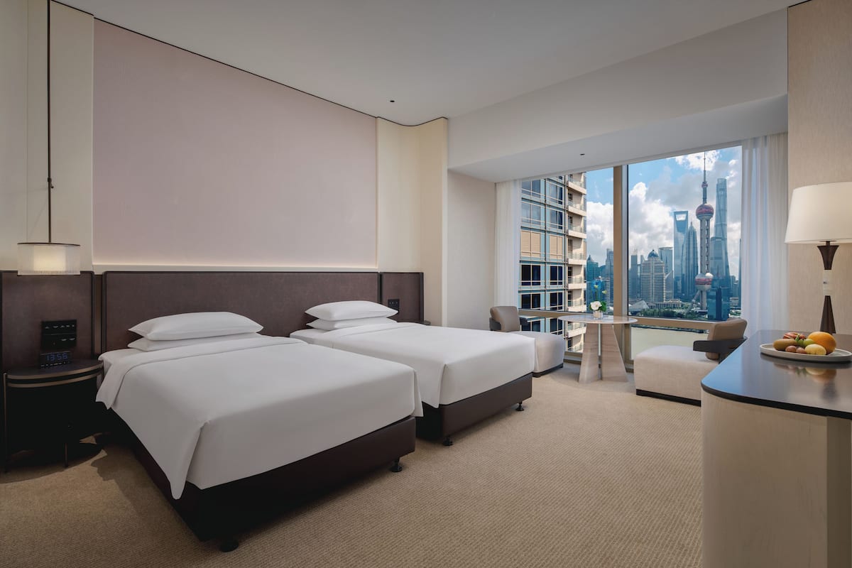 A hotel room with two beds, a desk, a chair, and a large window with a city view.