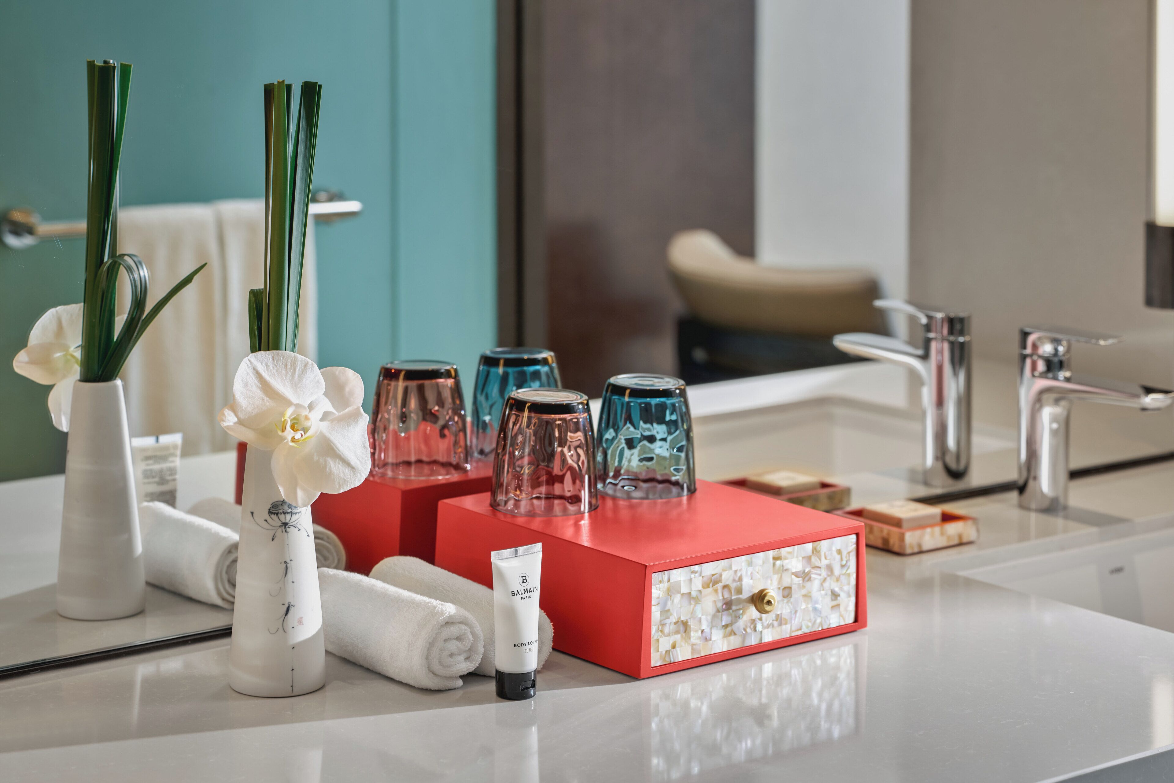 A bathroom with a white sink, a red box with toiletries, and a vase with white flowers.