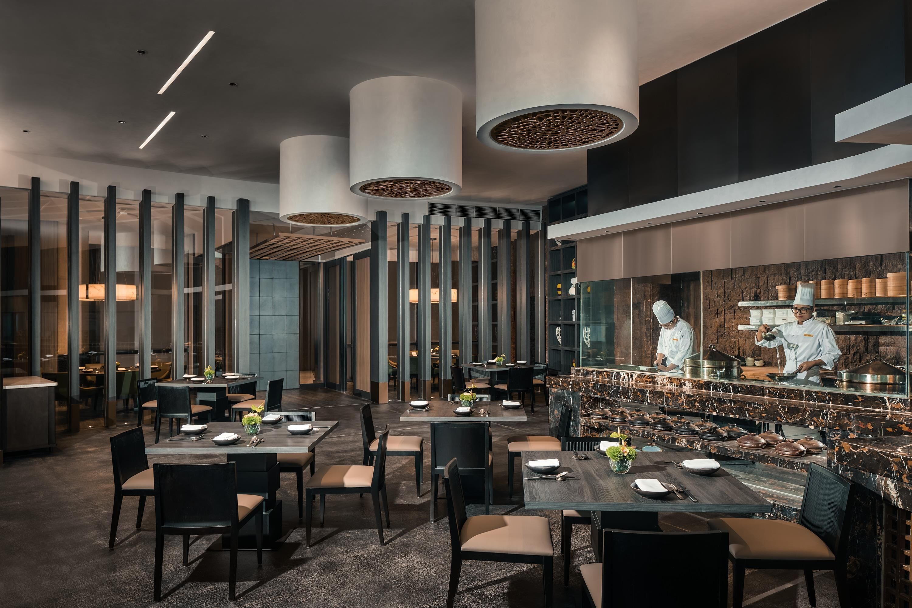 A modern restaurant interior with high ceilings, pendant lighting, and a central kitchen area.