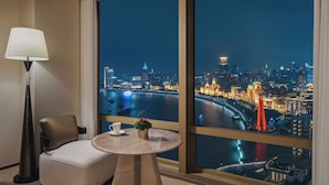 A hotel room with a large window offering a nighttime city view, a table with a cup and a small plant, and a modern lamp. - Hyatt on the Bund, Shanghai (Shanghai)