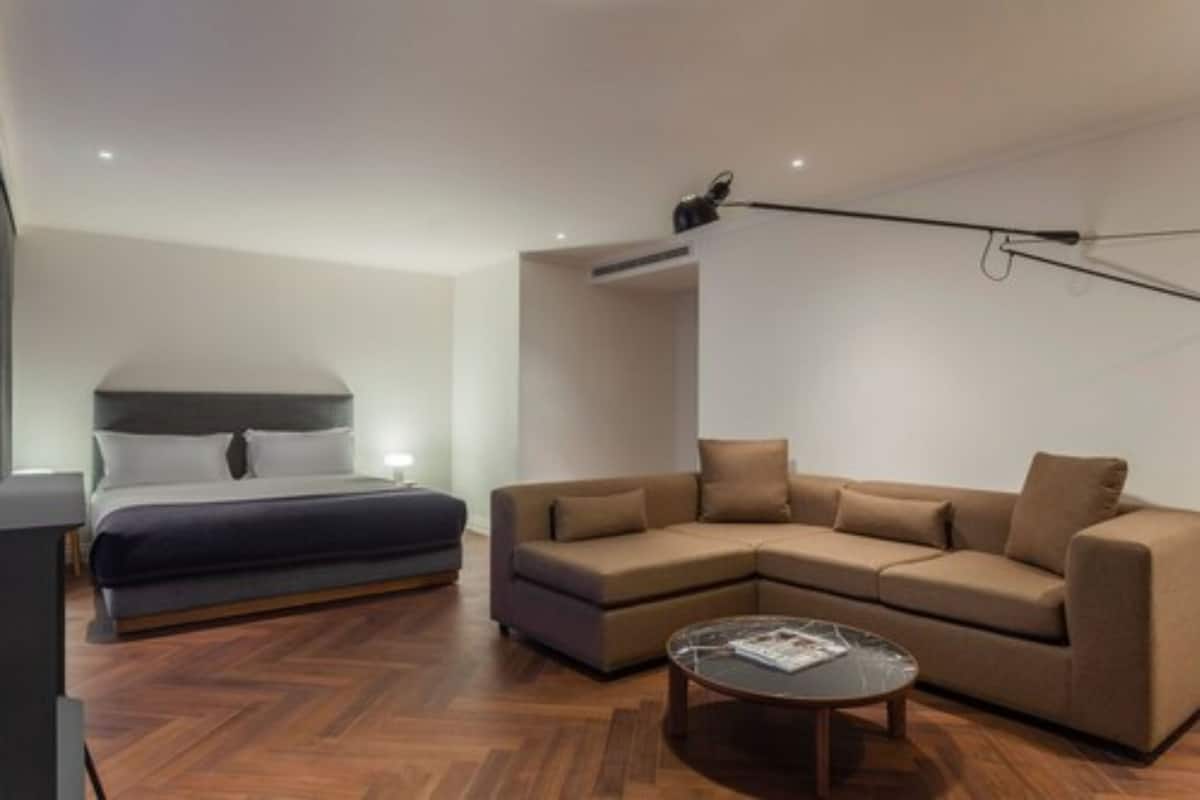 A modern hotel room with a bed, a sofa, a coffee table, and a ceiling-mounted projector.