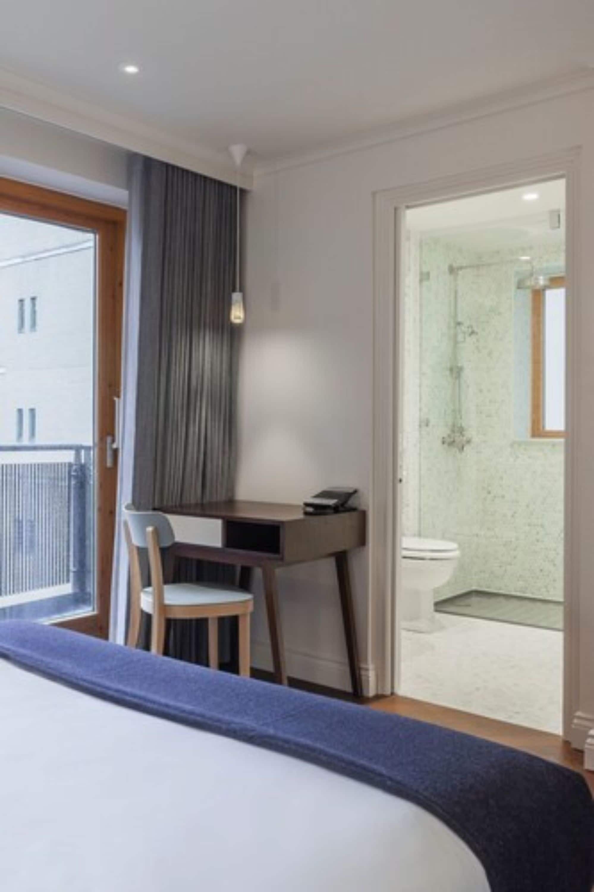 A hotel room with a bed, a desk, a chair, and a view of the bathroom.