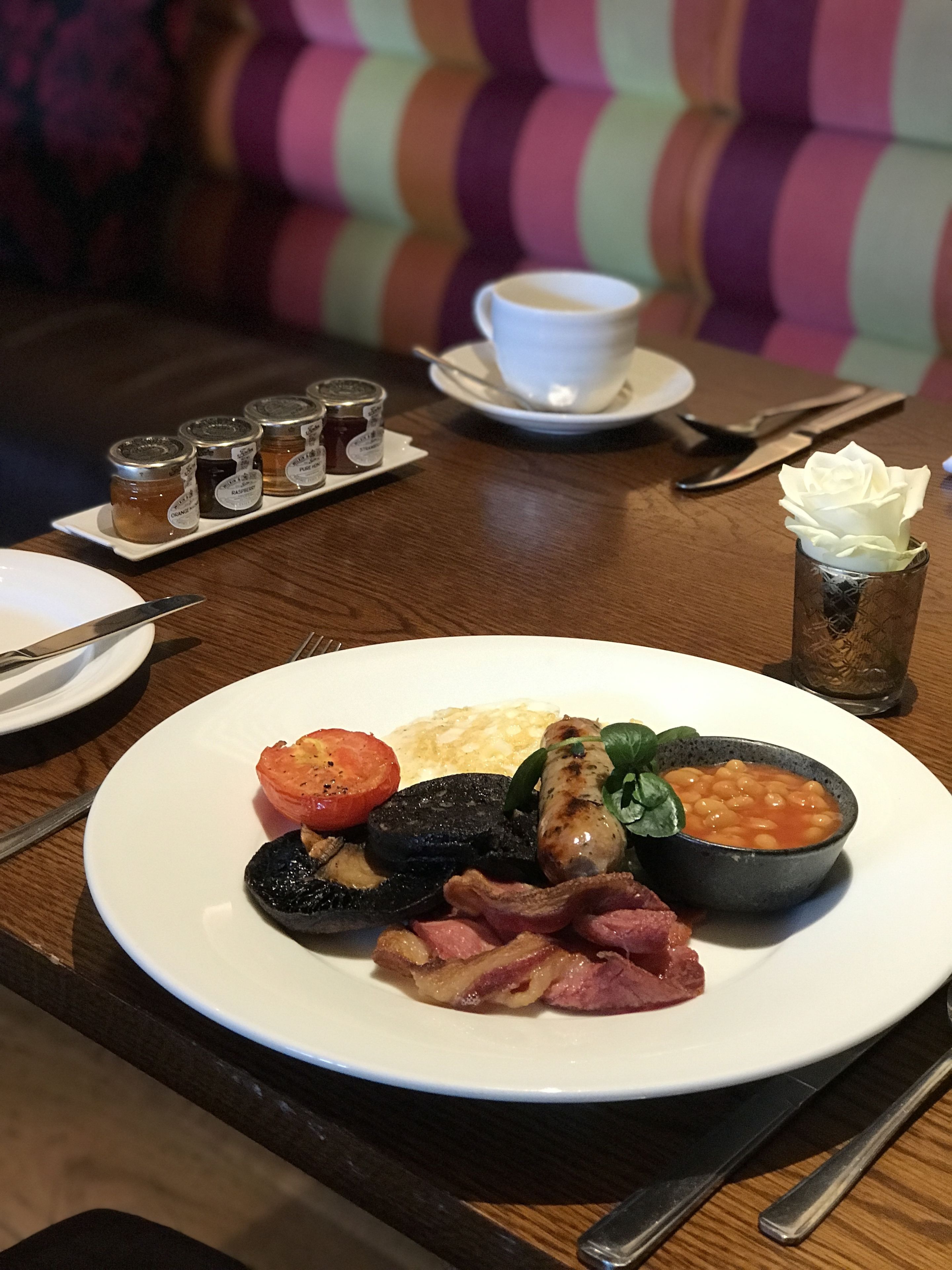 Un plato de desayuno con huevos, tocino, tomates, champiñones, frijoles y espinacas.