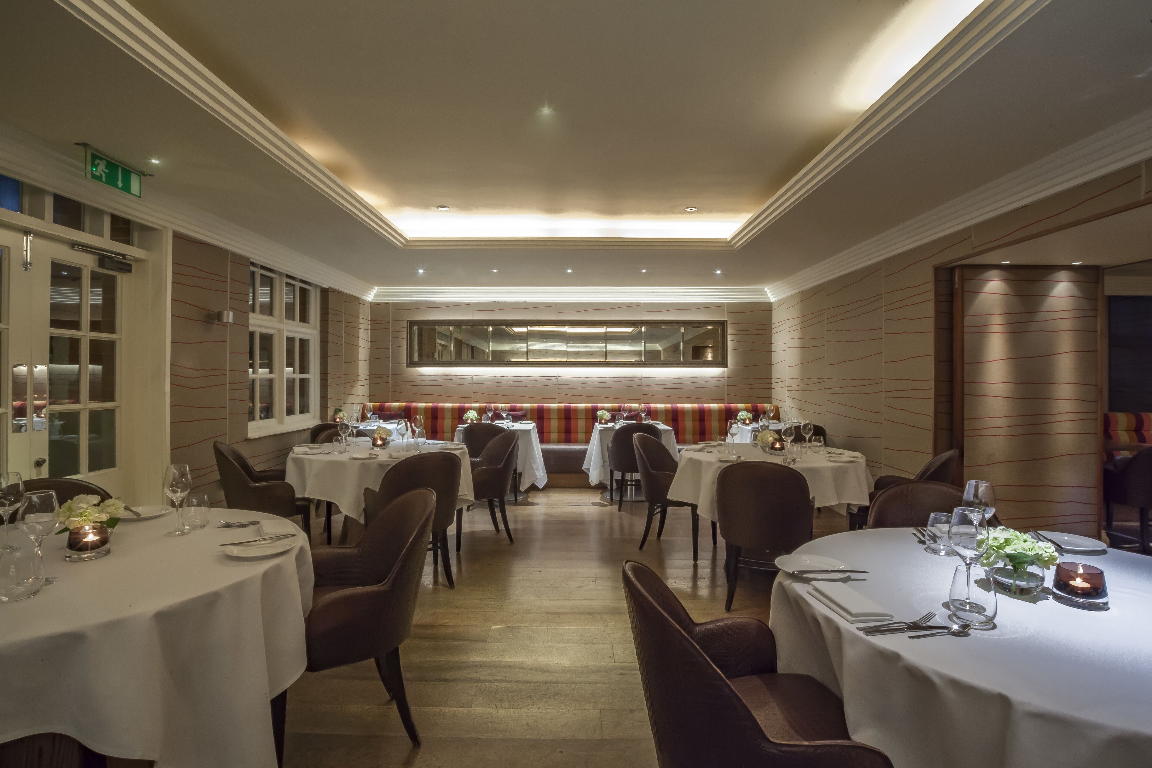 Un restaurante con varias mesas redondas, cada una con mantel blanco, sillas y cubertería.