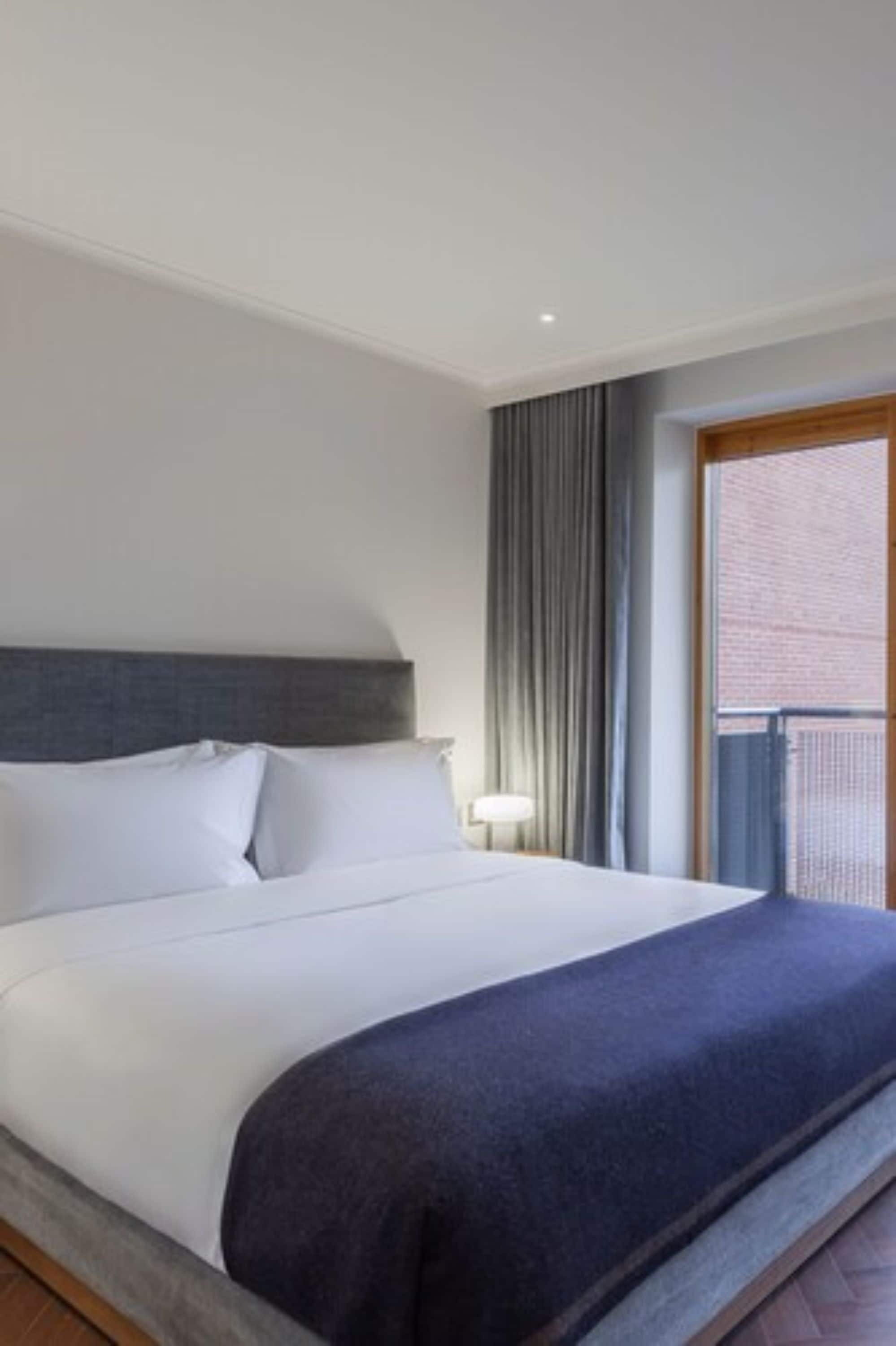 A hotel room with a large bed, a headboard, a window with curtains, and a view of the outside.