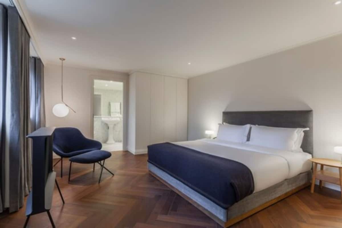 A modern hotel room with a large bed, a chair, a bedside table, and a hanging light fixture.