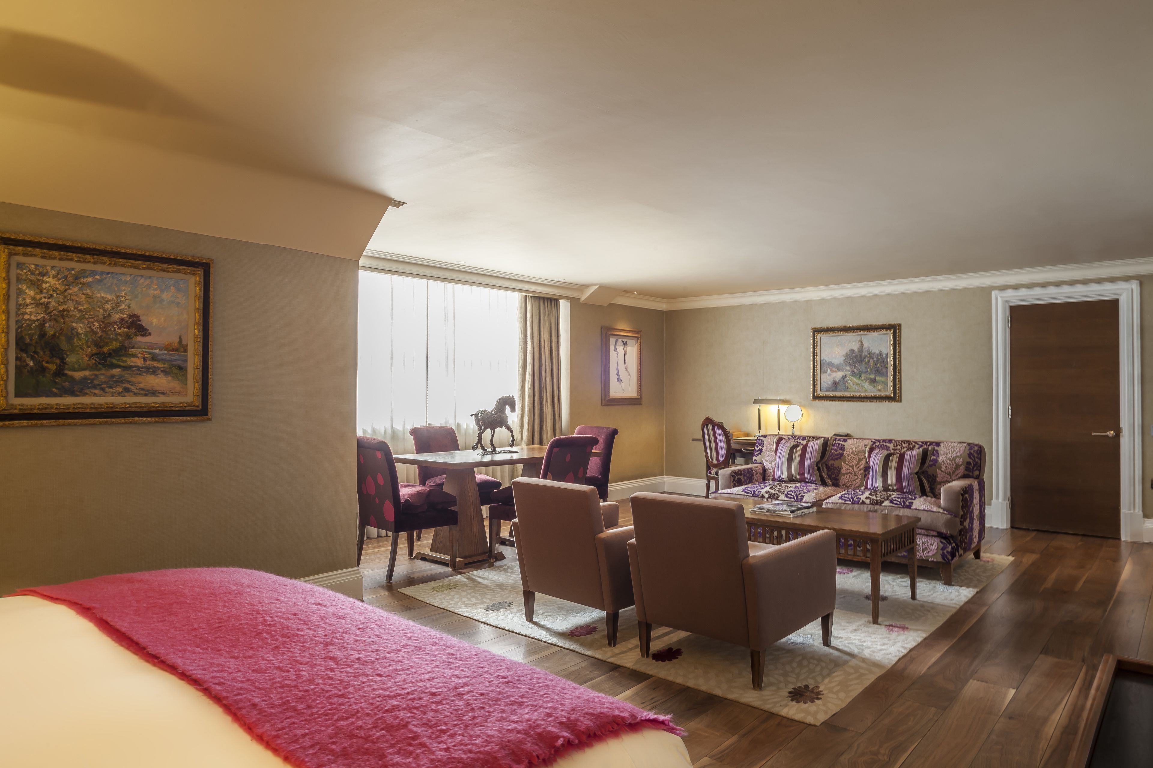 A hotel room with a bed, a dining table with chairs, a sofa, and a lamp.