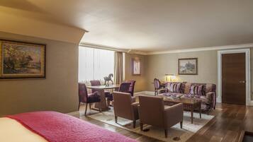 A hotel room with a bed, a dining table with chairs, a sofa, and a lamp.