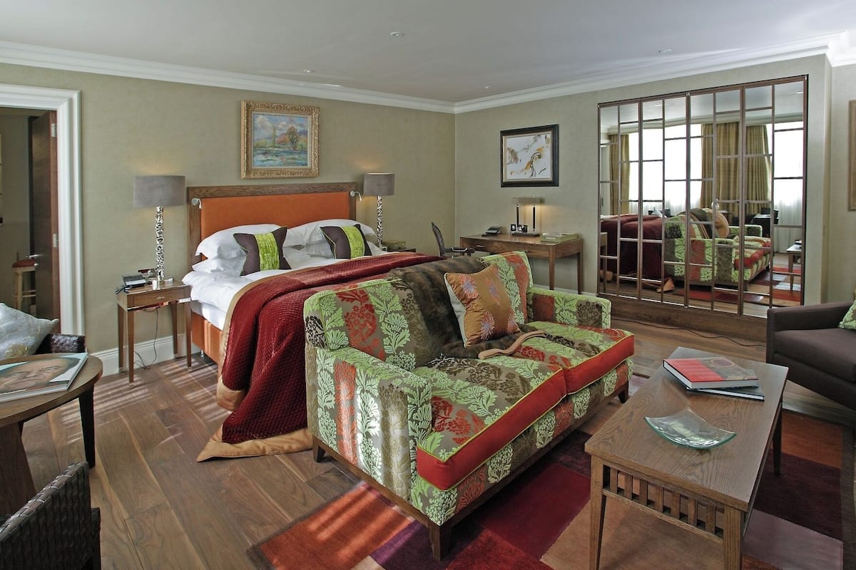 A hotel room with a bed, a sofa, a coffee table, a desk, and a mirror.