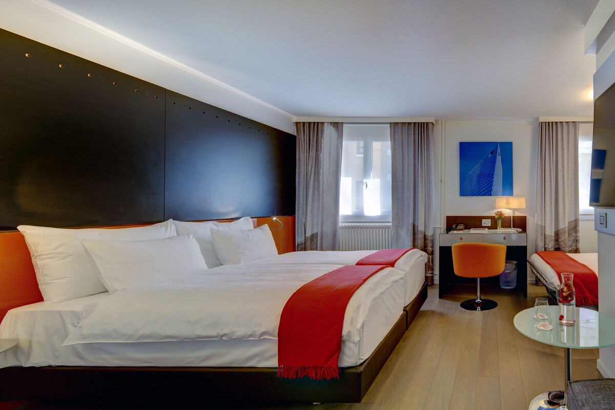 A hotel room with a large bed, a desk, a chair, a small table, and a TV.