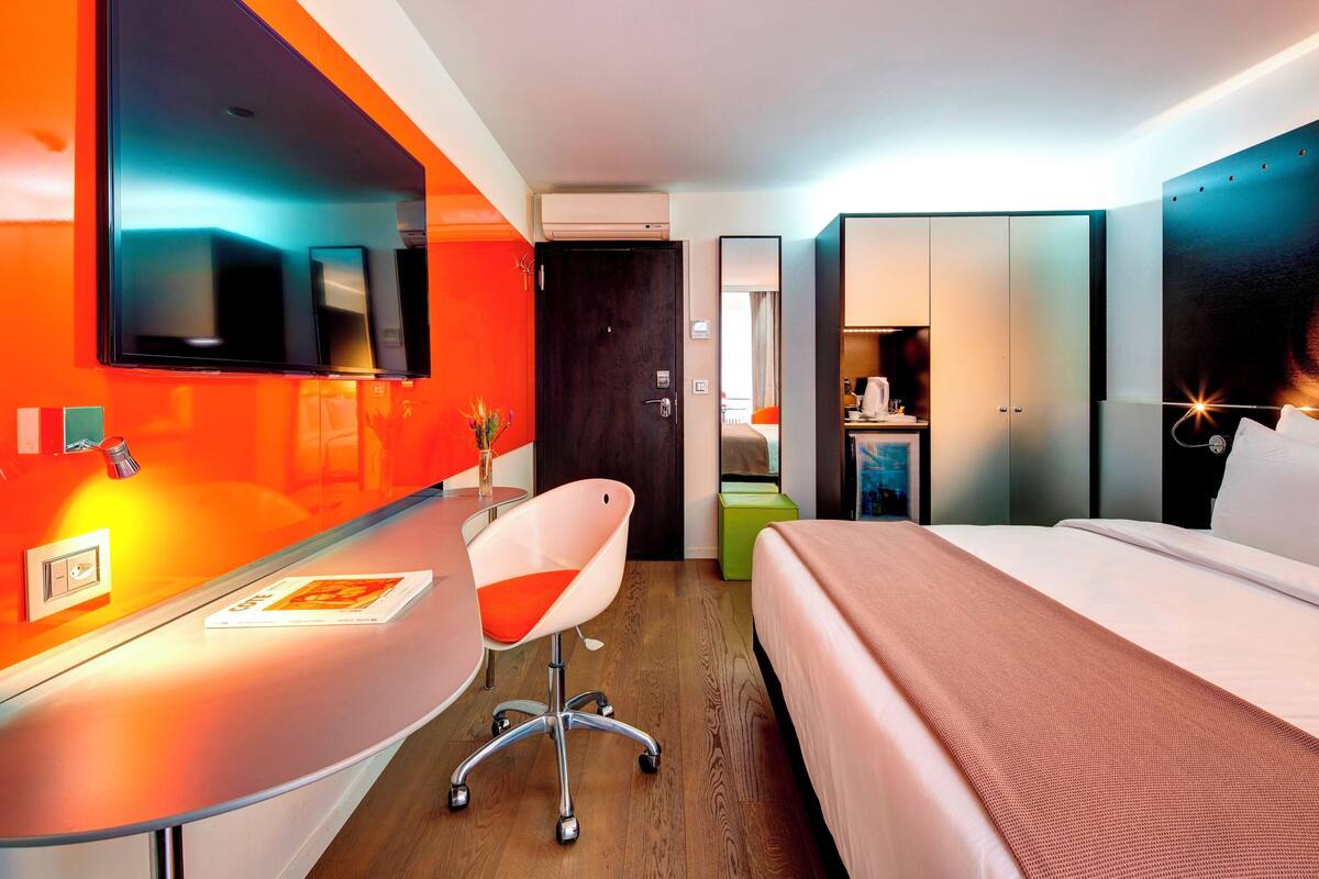 A modern hotel room with a bed, a desk, a chair, and a large mirror.