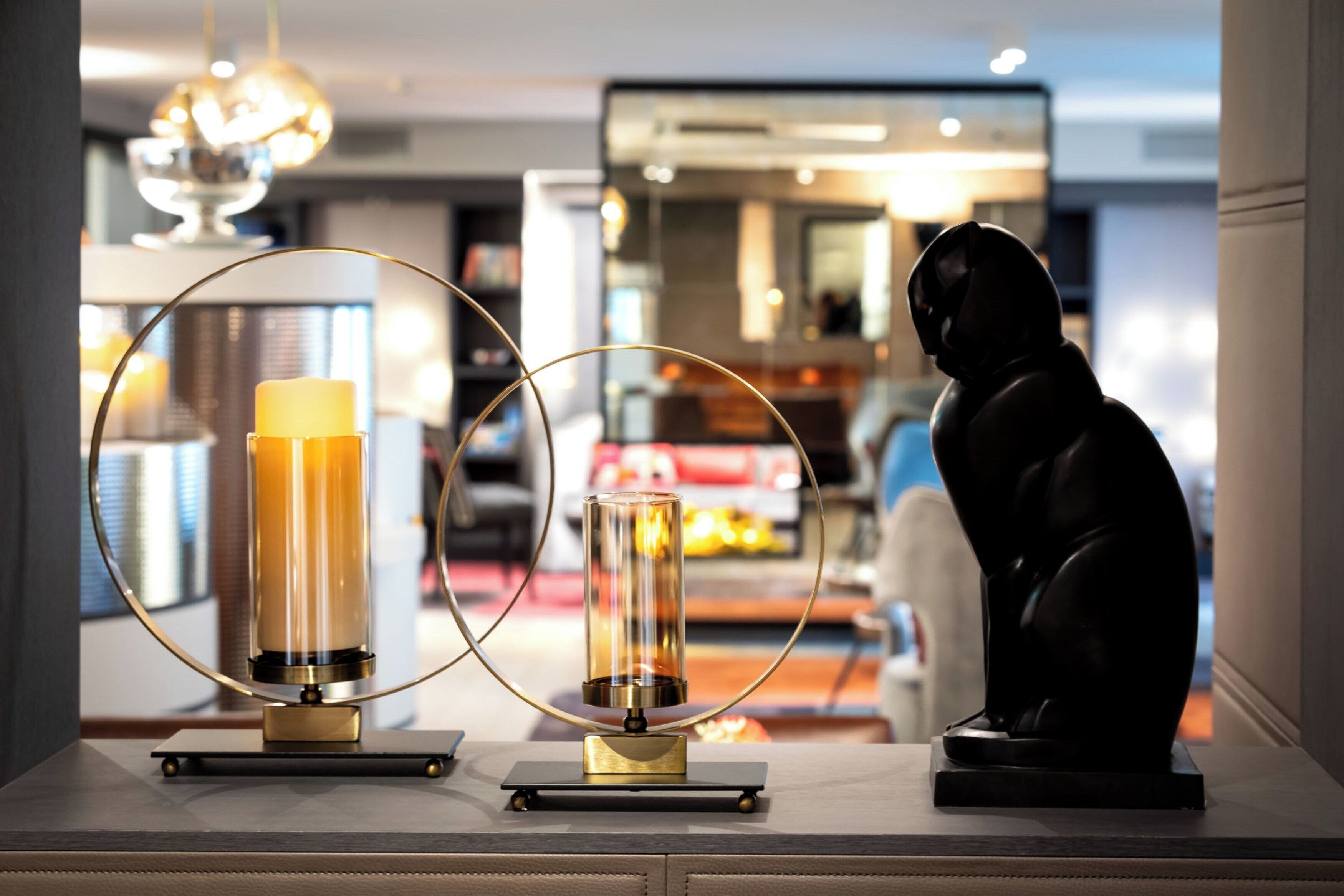 Un intérieur moderne agrémenté d’une sculpture, de deux objets cylindriques posés sur une table, et d’un arrière-plan flou évoquant un espace public.