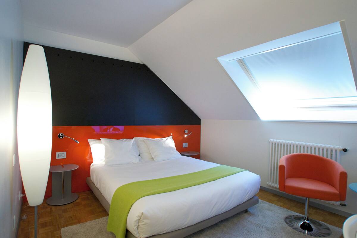 A modern bedroom with a bed, a chair, a lamp, and a skylight.