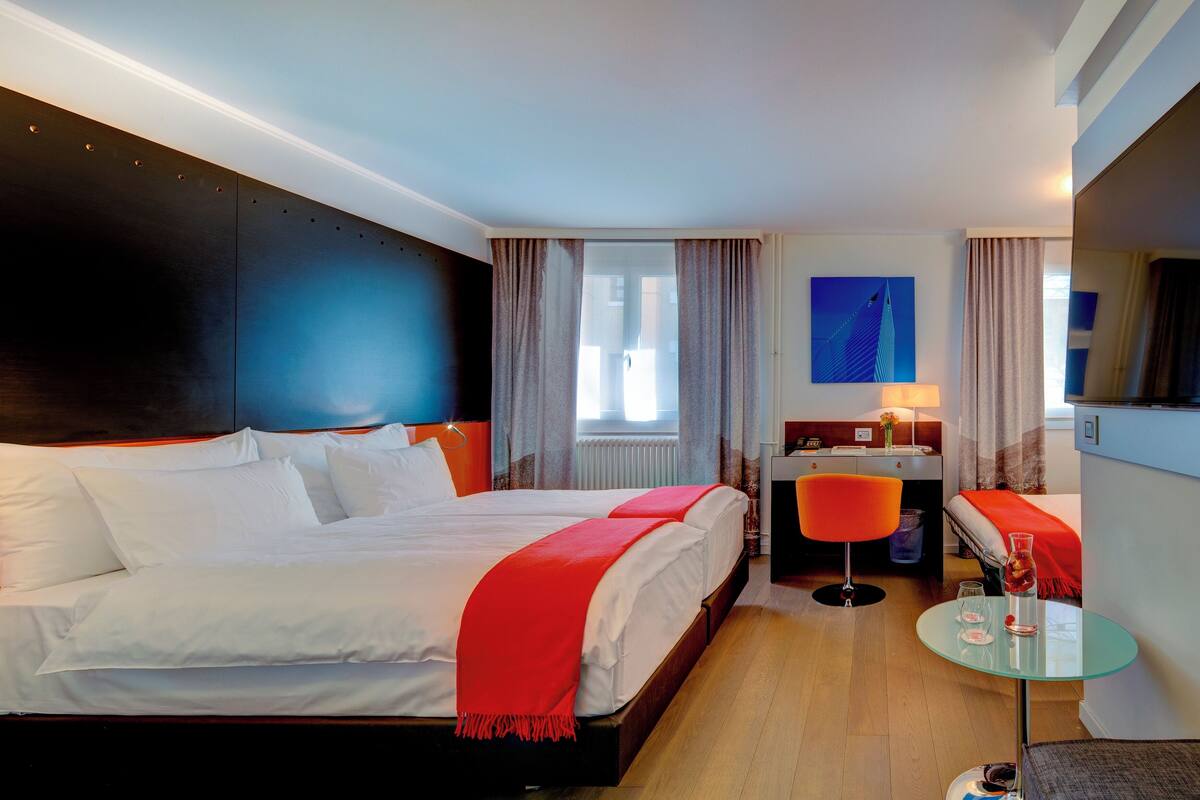 A hotel room with a large bed, a desk, a chair, and a small table with a glass.