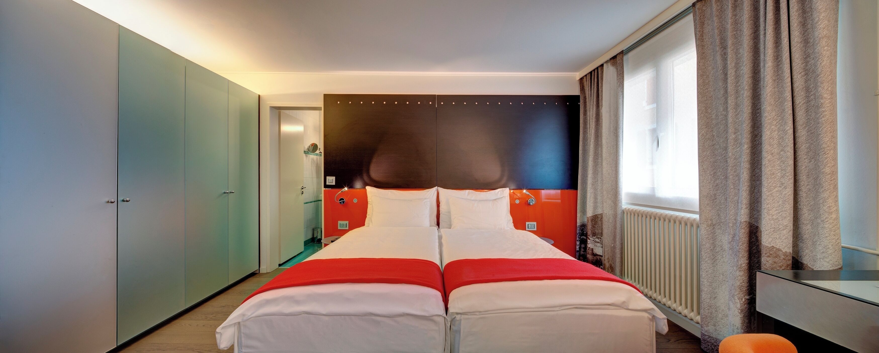 A hotel room with a large bed, a wardrobe, a bathroom, and a window with curtains.