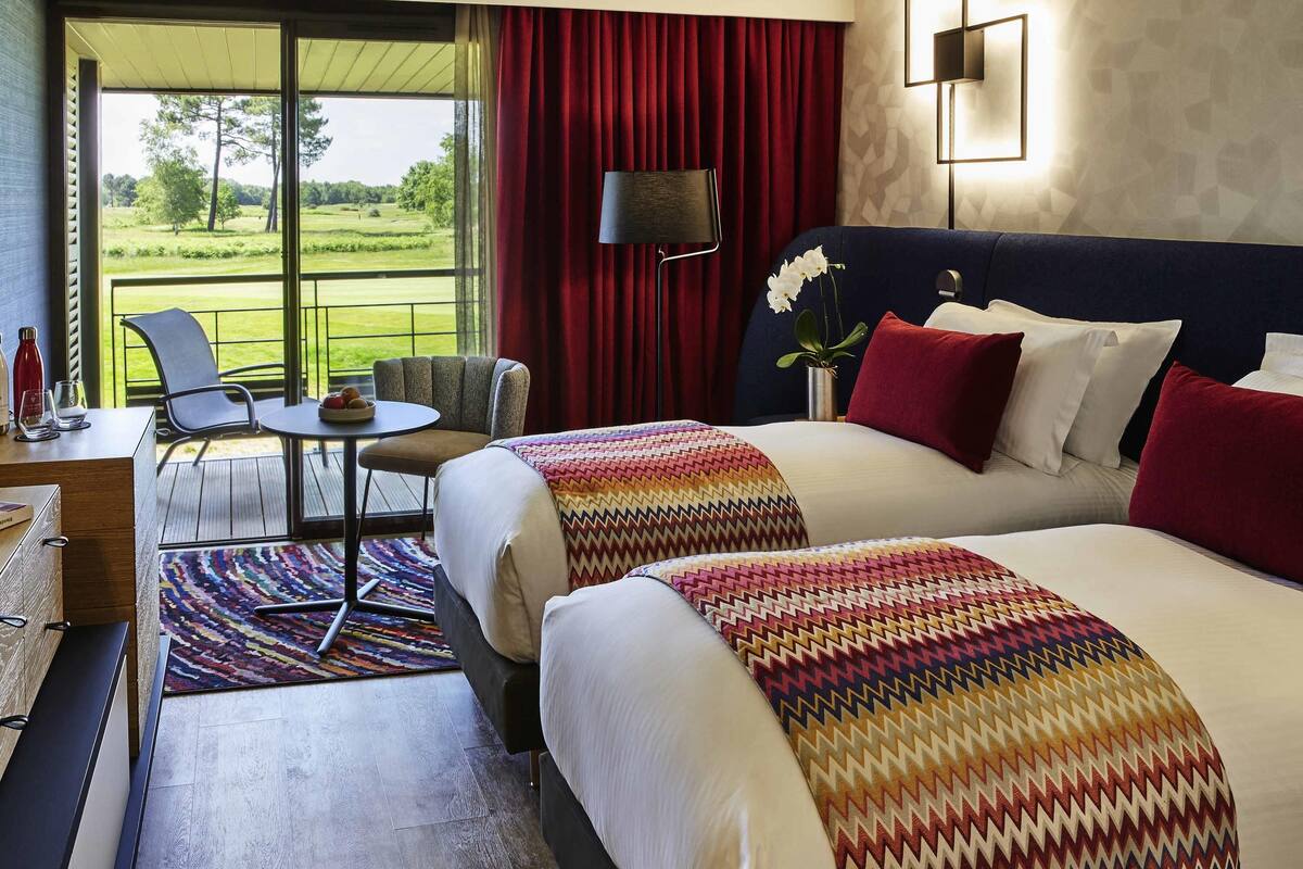 A hotel room with two beds, a desk, a chair, a lamp, and a view of a golf course.