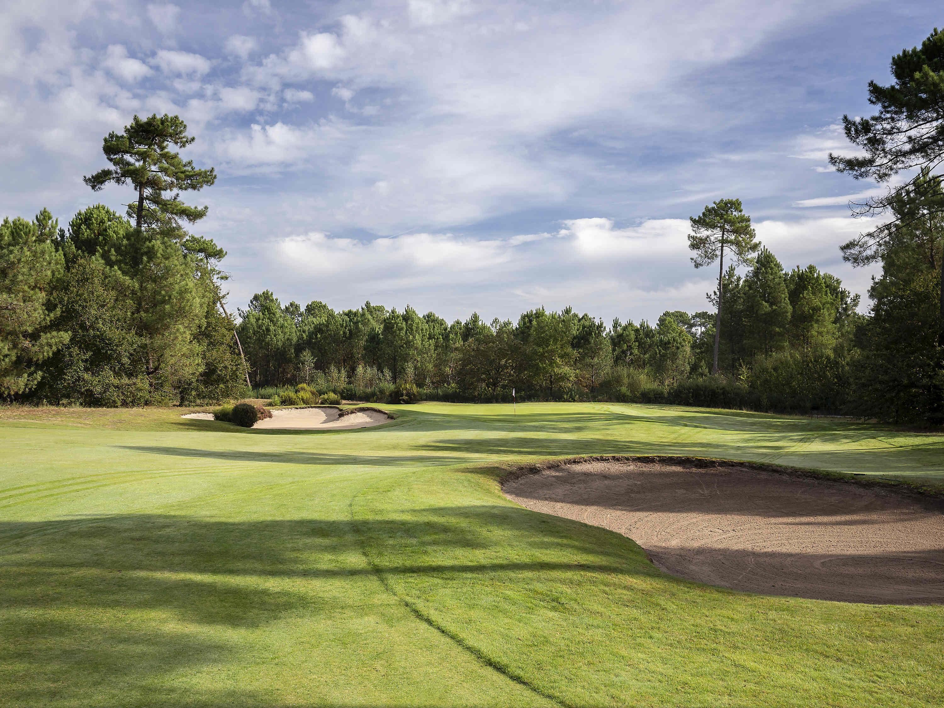 Un parcours de golf avec des bunkers de sable, un mât de drapeau et un ciel dégagé.